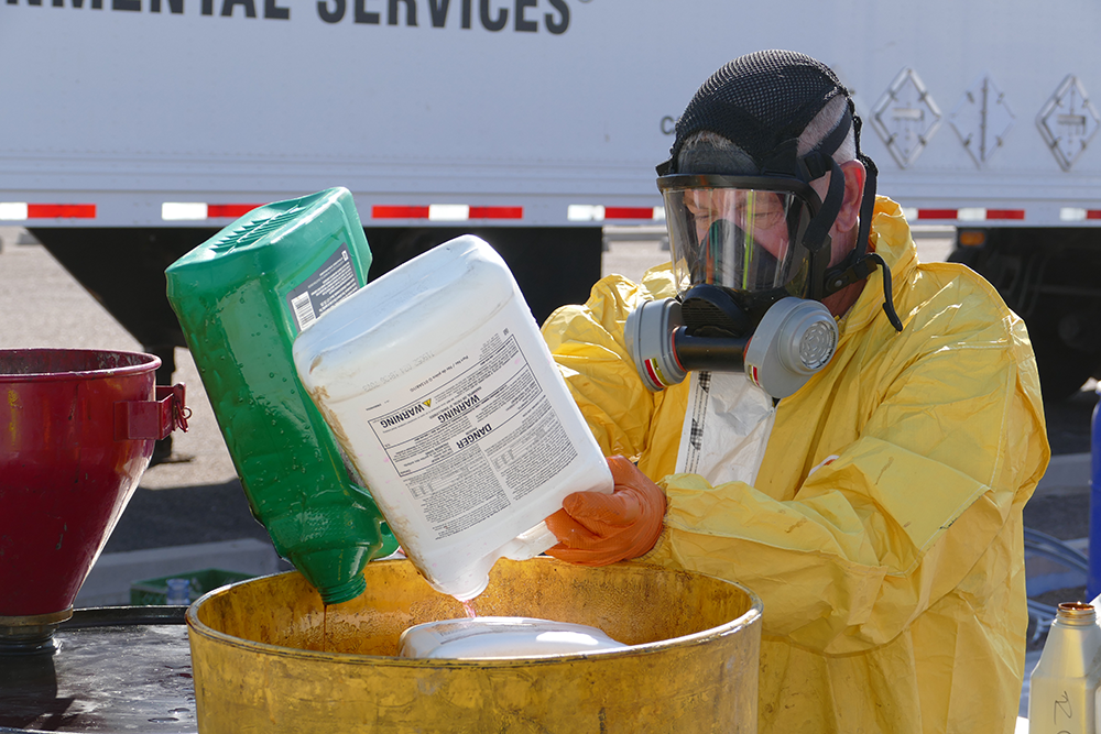 Waste technician pouring liquids into a barrel. He is wearing a protective suite.